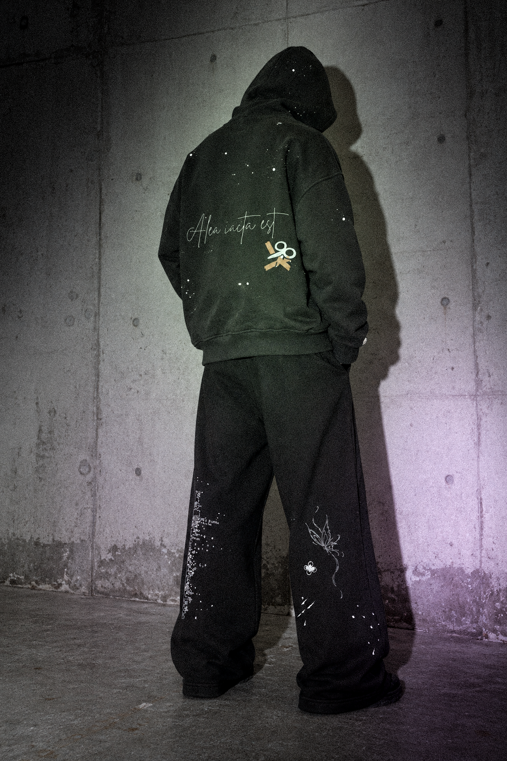 Look 006 — Alea hoodie and Route 00 sweatpants, hooded back view against a concrete wall.