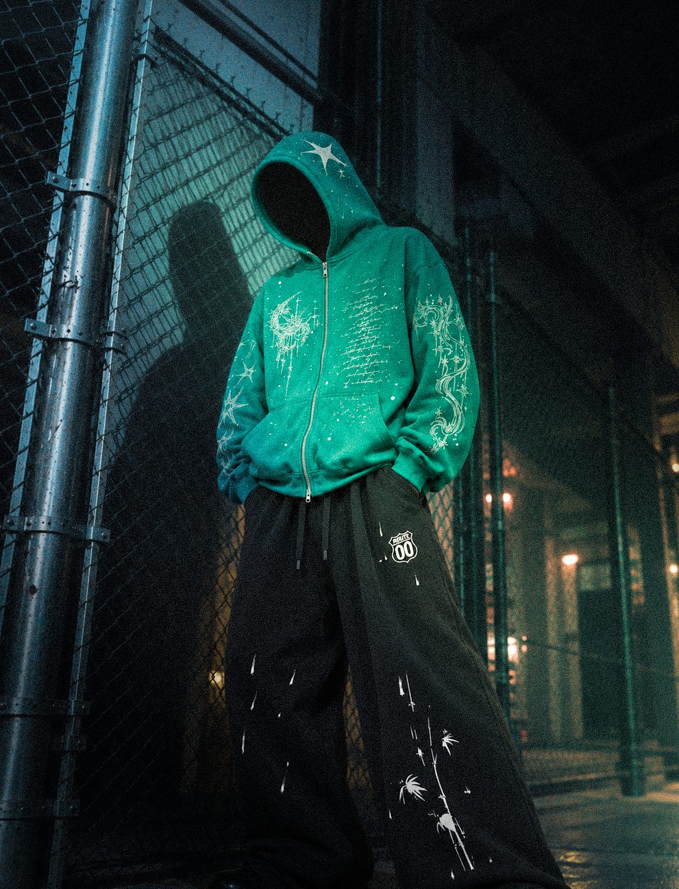 Look 008 — Blue Hour hoodie and Route 00 sweatpants, relaxed front view beside a chain-link fence.