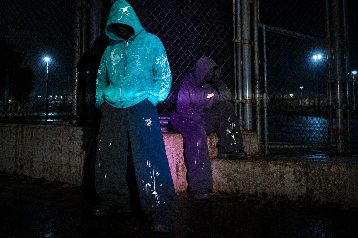 Look 009 — Two hooded models wearing Blue Hour and Alea with Route 00 sweatpants beside a night-time fence.